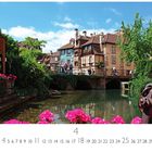 Colmar Klein Venedig. Ein malerischer Fluss mit Brücke, umliegende bunte Häuser, üppige Blumen und Bäume bei klarem Himmel.