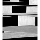 "Holocaust Denkmal" steht unter geometrischen, massiven Betonblöcken, die Schatten werfen und schlichte Strukturen bilden.