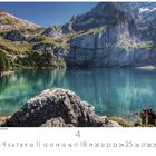 Schweiz, Oeschinensee, Kandersteg. Ein klarer, blauer See umgeben von Bergen, daneben stehen Menschen am Ufer.