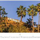 "HOLLYWOOD" in großen weißen Buchstaben auf einem Hügel, umgeben von Palmen und Bäumen unter klarem, blauem Himmel.