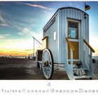 Strandwagen vor Sonnenuntergang, Kalender für April, großes Rad, gelbes Geländer, Fahne oben.