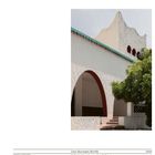 „Casa Gustavo Cristo“. Architektur mit weißen, gewellten Mauern, einem türkisfarbenen Dachrand und roten Bögen.