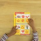 "Die Farbe Rot", "das Feuerwehrauto", "die Tomate", "die Kirschen". Kind blättert durch ein Lernbuch mit roten Symbolen.