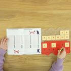 Heft mit "Ergänzungsaufgaben zur Addition", Zahlenkarten in Plastikhalterung, Hände bewegen eine Karte.