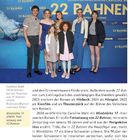 "22 Bahnen" mehrfach im Hintergrund. Gruppe von sieben Menschen, modisch gekleidet, posieren lächelnd.