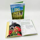 Aufrecht stehendes Buch: "ÖSTERREICHS schönste E-BIKE TAGES TOUREN". Daneben aufgeschlagen, zeigt Text und Bild.