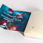 Ein offenes Buch mit Text: "Eine Leidenschaft, die dich verbrennen wird... mit sich reißt..." darauf bunte Blumen.
