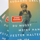 "SPIEGEL Bestseller", "Du musst meine Hand fester halten" auf einem Buchcover mit einem Kind in Latzhose.