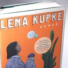 Zitat von Caroline Wahl: „Dieses Buch ist wie eine feste Umarmung, nachdem es einen richtig zerlegt hat.“ Illustration einer Person mit Tasse.