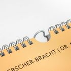 "DR. MED. PET." steht auf einem spiralförmig gebundenen, hellorangefarbenen Kalender.