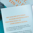 Text: "DIE GESCHICHTE EINER AUSSERGEWÖHNLICHEN FREUNDSCHAFT IN UNSICHEREN ZEITEN." Hintergrund in hellem Blau.