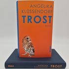 ANGELIKA KLÜSSENDORF TROST. Auf orangefarbenem Buch ein Vogel. Darunter liegt ein blaues Buch mit gleichen Texten.