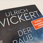 „Ulrich Wickert“, „Der Raub“, rotes Label „Spiegel Bestseller-Autor“, umrahmt von einem Dach im Hintergrund.
