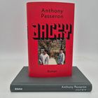 Der Text "Anthony Passeron JACKY Roman". Abbildung: Zwei Jungen vor Bäumen, roter Hintergrund, Buch auf grauem Band.