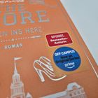 Text: „THE CORE – MITTEN INS HERZ – ROMAN“, Sticker: „SPIEGEL Bestseller-Autorin“. Rubrik „Off Campus“, Prime-Logo. Abbildungen: Gebäude, High Heels, Marmeladenglas.
