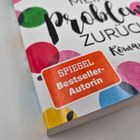 Text: „SPIEGEL Bestseller-Autorin“, „Mein Problem Zurück“, „Roman“. Bunte Kreise als Hintergrund.