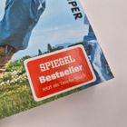Text: „SPIEGEL Bestseller Jetzt als Taschenbuch“. 

Ein Mann in brauner Hose und blauem Shirt vor Landschaft.