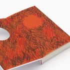 Ein aufgeschlagenes Buch mit orangefarbenem Cover, bedeckt von schwarzen und roten Kritzeleien, und einem runden Loch.