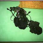 Ich kann keine Texte im Bild erkennen. Schwarze, gemusterte Stoffe liegen auf einem grünen Untergrund, im Hintergrund ein gemustertes Kissen.