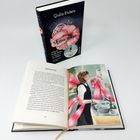 Ein aufgeschlagenes Buch zeigt Text auf der linken Seite, rechts eine Illustration einer Person in einer Küche. Ein zweites Buch steht dahinter.