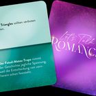 Zwei Spielkarten: Links mit Text "Love Triangles sollten verboten werden." und "Fated-Mates-Trope...". Rechts lila mit "Let's Talk Romance".