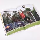 Texte: Puma. Ein junger Torwart springt im roten Trikot auf einem Fußballplatz, um einen Ball zu fangen.