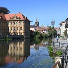 Eine historische Stadtansicht mit Fluss, einem großen alten Gebäude links und einer malerischen Uferpromenade rechts.