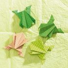 Vier Origami-Frösche in Grün- und Orangetönen mit Mustern auf hellgrünem Hintergrund.