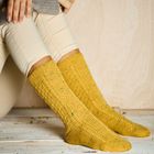 Keine Texte zu erkennen. Eine Person trägt gelbe, gestrickte Socken und sitzt mit Beinen angewinkelt auf einem Holzboden.