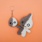 Zwei gehäkelte Figuren, grau und weiß, auf orangefarbenem Hintergrund: ein Schlüsselanhänger und eine größere Figur.