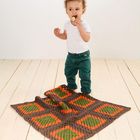 Es gibt keinen Text. Ein Kind isst einen Keks, trägt ein weißes T-Shirt und grüne Hose, steht auf einem Holzboden.