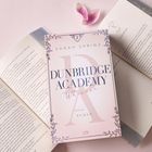 Auf einem Buchcover steht "DUNBRIDGE ACADEMY Whoever". Daneben liegen zwei geöffnete Bücher und rosa Blütenblätter.