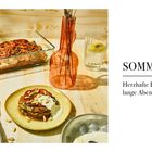 SOMMER: Herzhafte Düfte, lange Abende. Gericht, Gemüse, Vase mit Zweigen, Glas mit Limettenscheibe auf hellem Tisch.