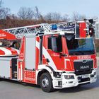 "Berliner Feuerwehr", "FEUERWEHR", "112". Ein rotes Feuerwehrfahrzeug mit Leiter und Korb auf einem Parkplatz.