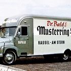 Aufschrift: "Dr. Bald & Muster­ring-Möbel, Kassel-Am Stern". Der Lastwagen ist vintage, geparkt neben einem Gebäude.