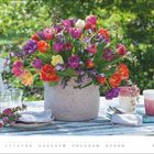 APRIL. Kalenderseite mit buntem Tulpenstrauß auf einem Tisch, daneben Tassen und Gläser im Garten.