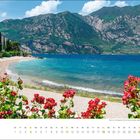 April-Kalender mit Strandblick, Bergen im Hintergrund, blauer Himmel, rot blühende Rosen im Vordergrund.