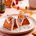 Essbare Häuschen aus Keksen mit bunten Streuseln und Gummibärchen, daneben eine Tasse mit heißem Getränk.