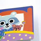 Ein illustriertes Kinderbuch zeigt einen Waschbären im Bett mit einem Teddybär und einem Buch mit einem Vogelbild.