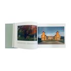 Ein geöffnetes Buch zeigt links einen Baum mit rotem Laub, rechts ein symmetrisches Gebäude mit zwei Türmen und blauem Himmel.