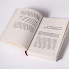 Links: "Hast du je deine Bedürfnisse... um jemand anderen glücklich... obwohl es sich so angefühlt hat?" Rechts: "Wir glauben an den Mythos der Perfektion". Ein aufgeschlagenes Buch liegt vor einem weißen Hintergrund.