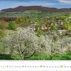April 2023 Kalenderblatt mit blühender Frühlingslandschaft, blühenden Obstbäumen, grünen Hügeln und einem kleinen Dorf.