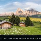 4 APR. Zwei Holzhütten auf einer grünen Wiese, umgeben von Bäumen, mit beeindruckenden Bergen im Hintergrund.