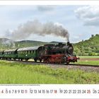 April-Kalenderblatt mit einer alten Dampflokomotive auf einer Eisenbahnstrecke, umliegende grüne Landschaft und Wald.