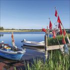 Ein ruhiger Fluss mit kleinen Booten. Rote Fahnen wehen im Wind. Boote mit Ausrüstung an einem Pfahl befestigt.