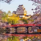 Kalenderblatt mit April 2023. Kirschblüten, eine alte japanische Burg und ein roter Holzsteg spiegeln sich im Wasser.