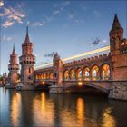 Ein roter Backsteinbogen mit Türmen über einem Fluss bei Dämmerung, beleuchtet, mit einem Zug, der darüber fährt.
