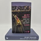 Buchcover mit Text: "HELMUT KRAUSSER WER HAT UNS JE GELIEBT? ROMAN". Darstellung einer beleuchteten Stadt und Brücke bei Nacht.