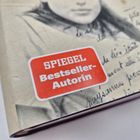 „SPIEGEL Bestseller-Autorin“ auf rotem Sticker; Schwarz-Weiß-Foto einer Frau mit Text im Hintergrund.