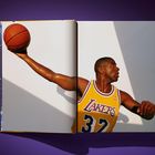 Der Text "Lakers 32" ist auf einem gelben Basketball-Trikot. Eine Person hält einen Basketball in ausgestrecktem Arm.